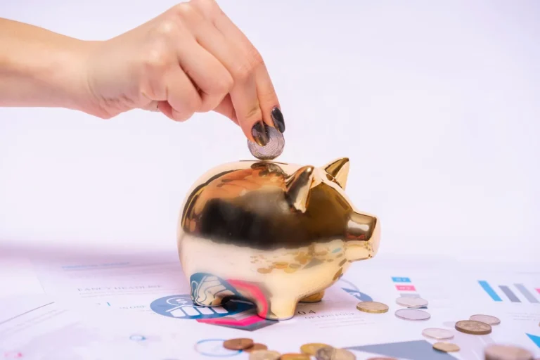 When Central Banks Move Rates, What Changes at Home? A hand places a coin into a golden piggy bank surrounded by financial documents.